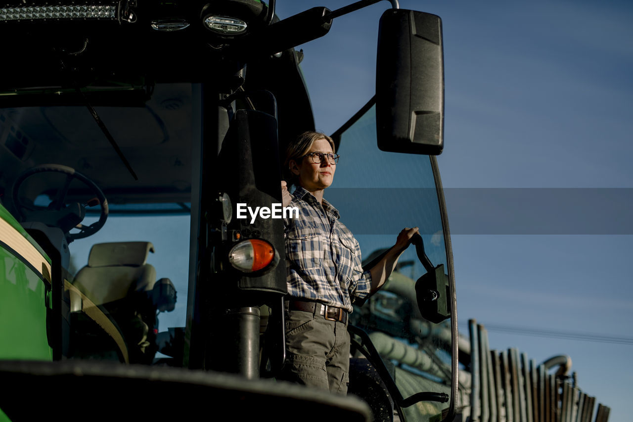 Contemplative farmer standing on tractor at farm