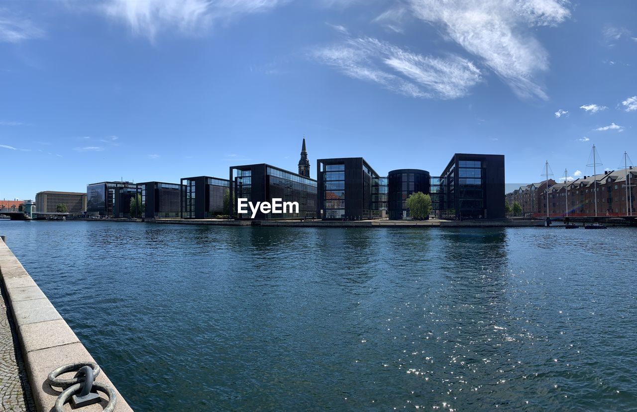 MODERN BUILDINGS BY RIVER AGAINST SKY