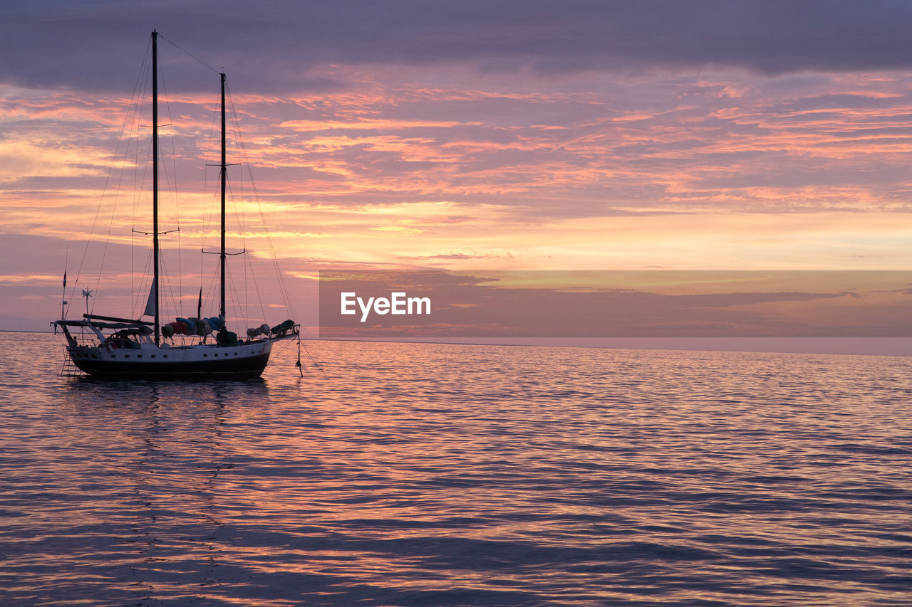 Sailing boat on sea against cloudy sky during sunset