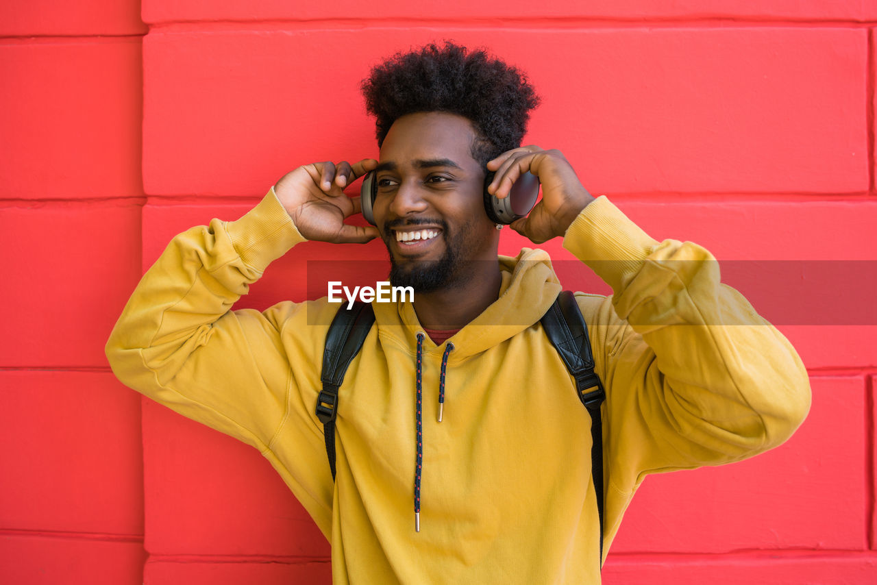 Smiling young man listening music against red wall