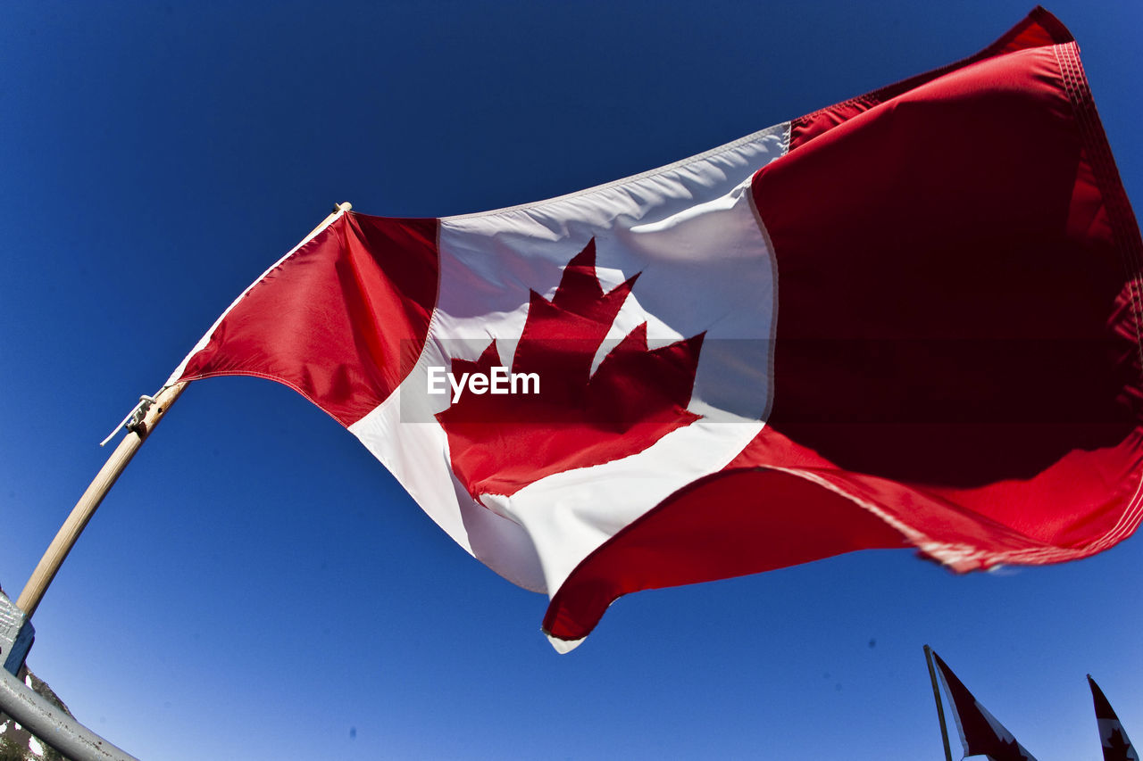 Low angle view of canadian flag against clear blue sky