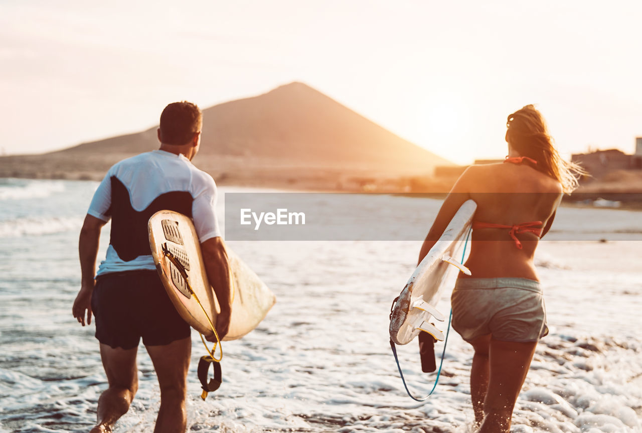 Happy friends carrying surfboards while walking on shore at beach