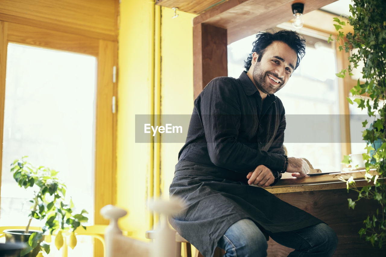 Portrait of happy waiter sitting on stool