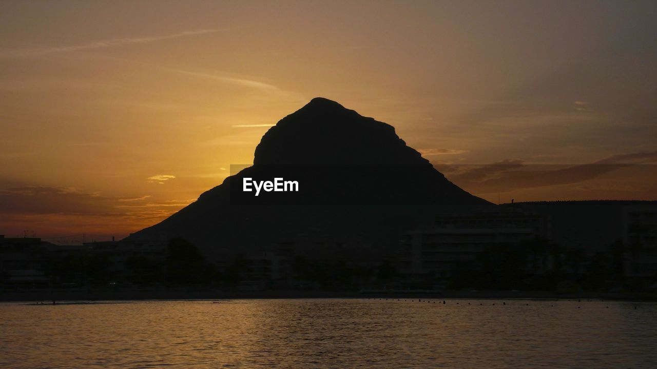 SILHOUETTE MOUNTAINS BY SEA AGAINST ORANGE SKY