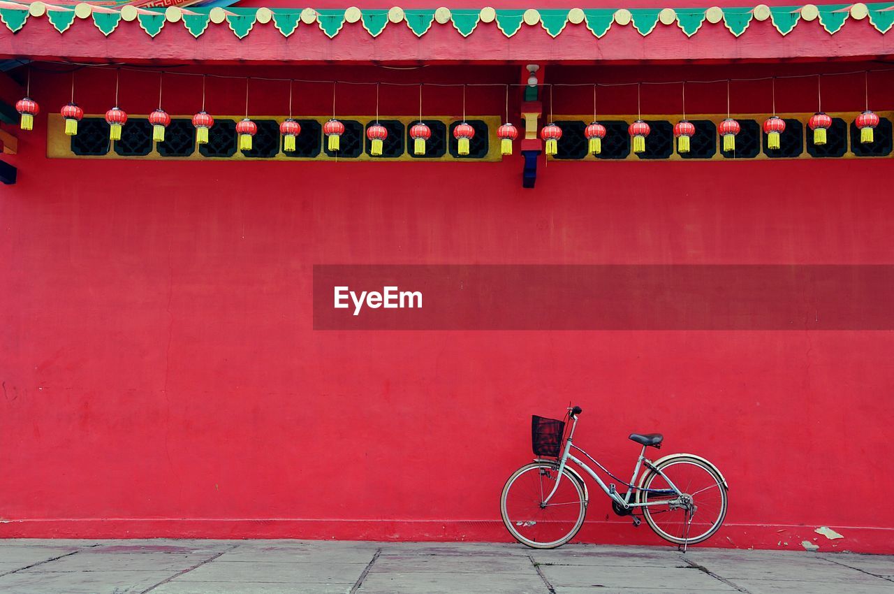 Bicycle parked on street against red wall
