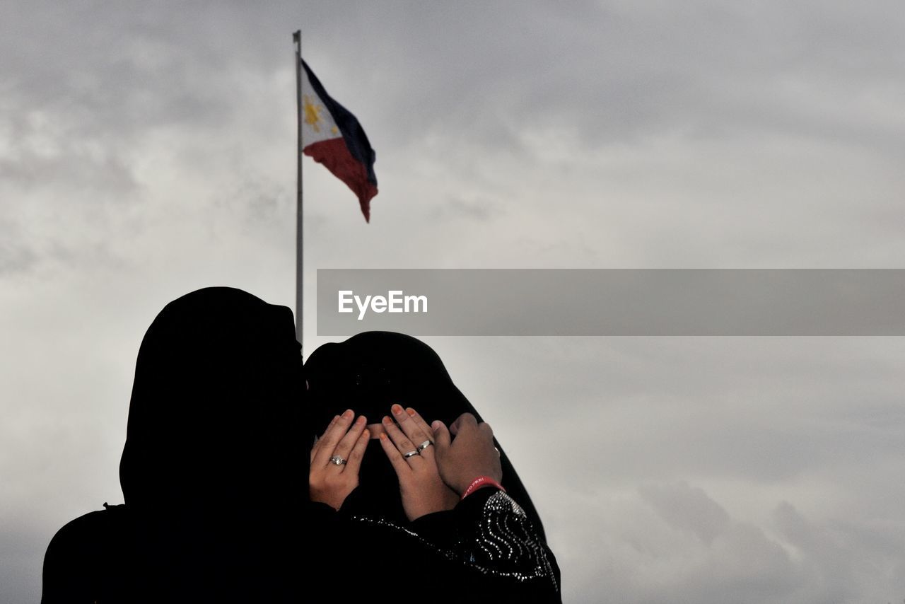 Rear view of woman in burka consoling friend against philippines flag