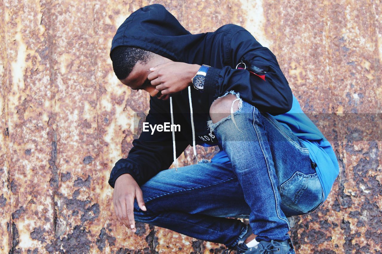 Young man crouching and looking down against metal wall