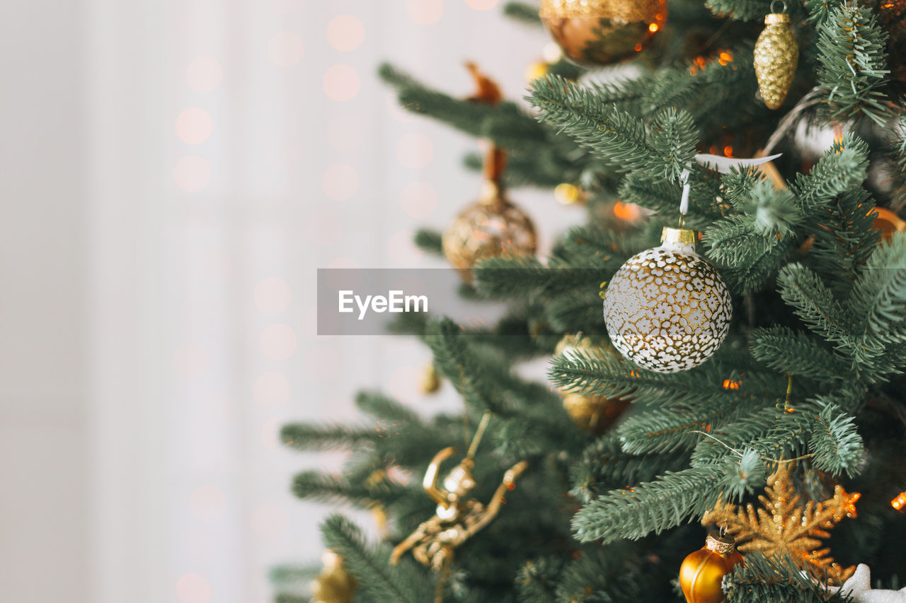 Decorated christmas tree in golden and white toys with lights bokeh textured background