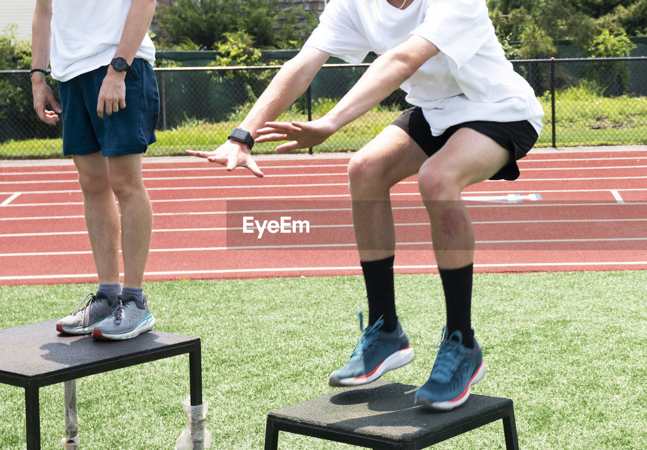 Athletes at a summer sports camp jumping onto different size plyo boxes outdoors on a turf field,