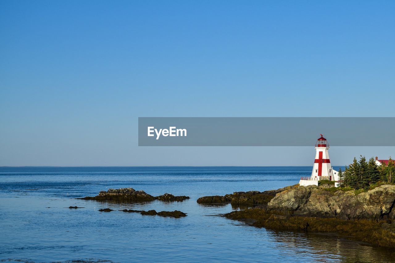Lighthouse by sea against clear sky