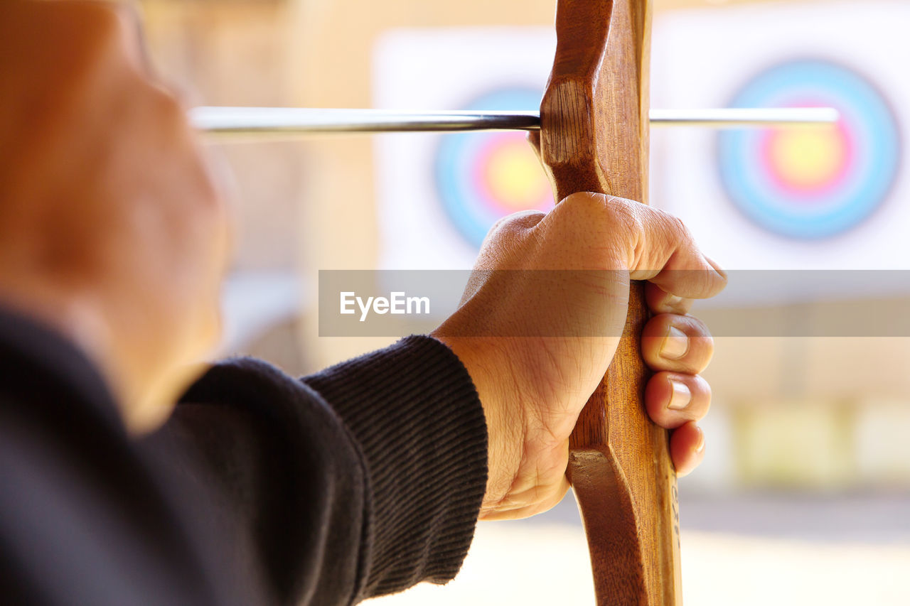 Close-up of man with bow and arrow aiming at target