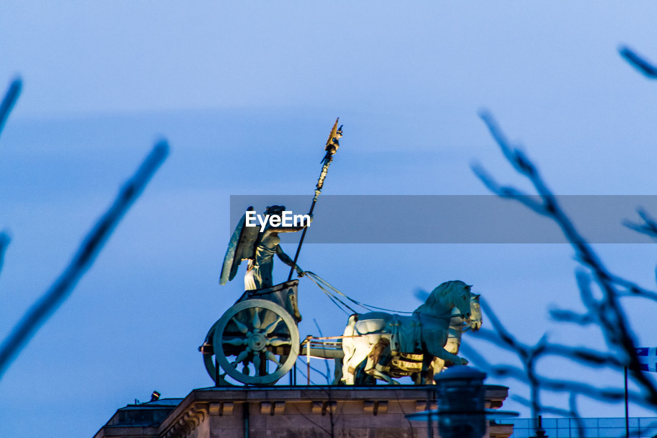 Low angle view of illuminated statue on brandenburg gate against sky at dusk