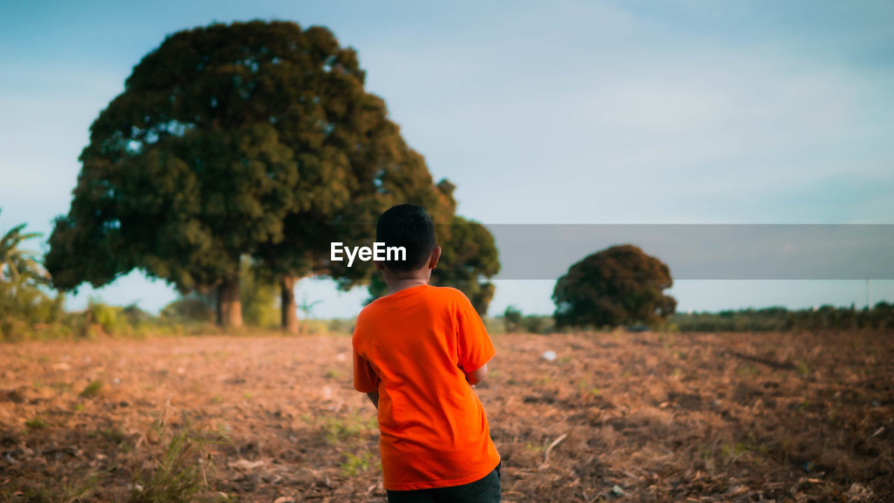 REAR VIEW OF BOY ON FIELD AGAINST TREES