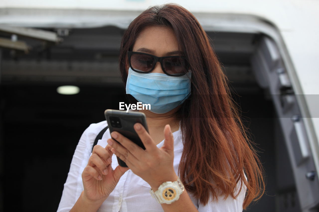 PORTRAIT OF YOUNG WOMAN USING MOBILE PHONE IN BUS