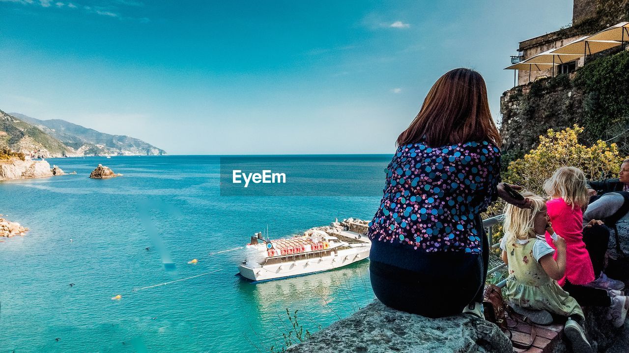 REAR VIEW OF PEOPLE LOOKING AT SEA BY BOAT