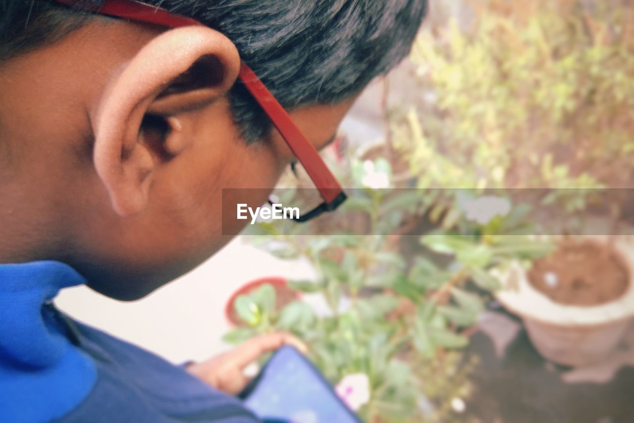 Close-up of boy using mobile phone against plants