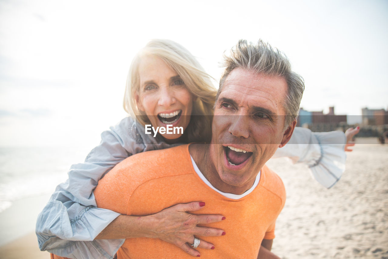 Close-up of man giving piggyback ride to happy girlfriend standing at beach