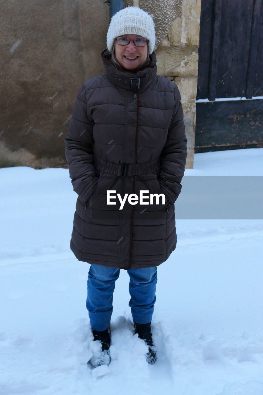 Full length portrait of smiling woman standing on snow