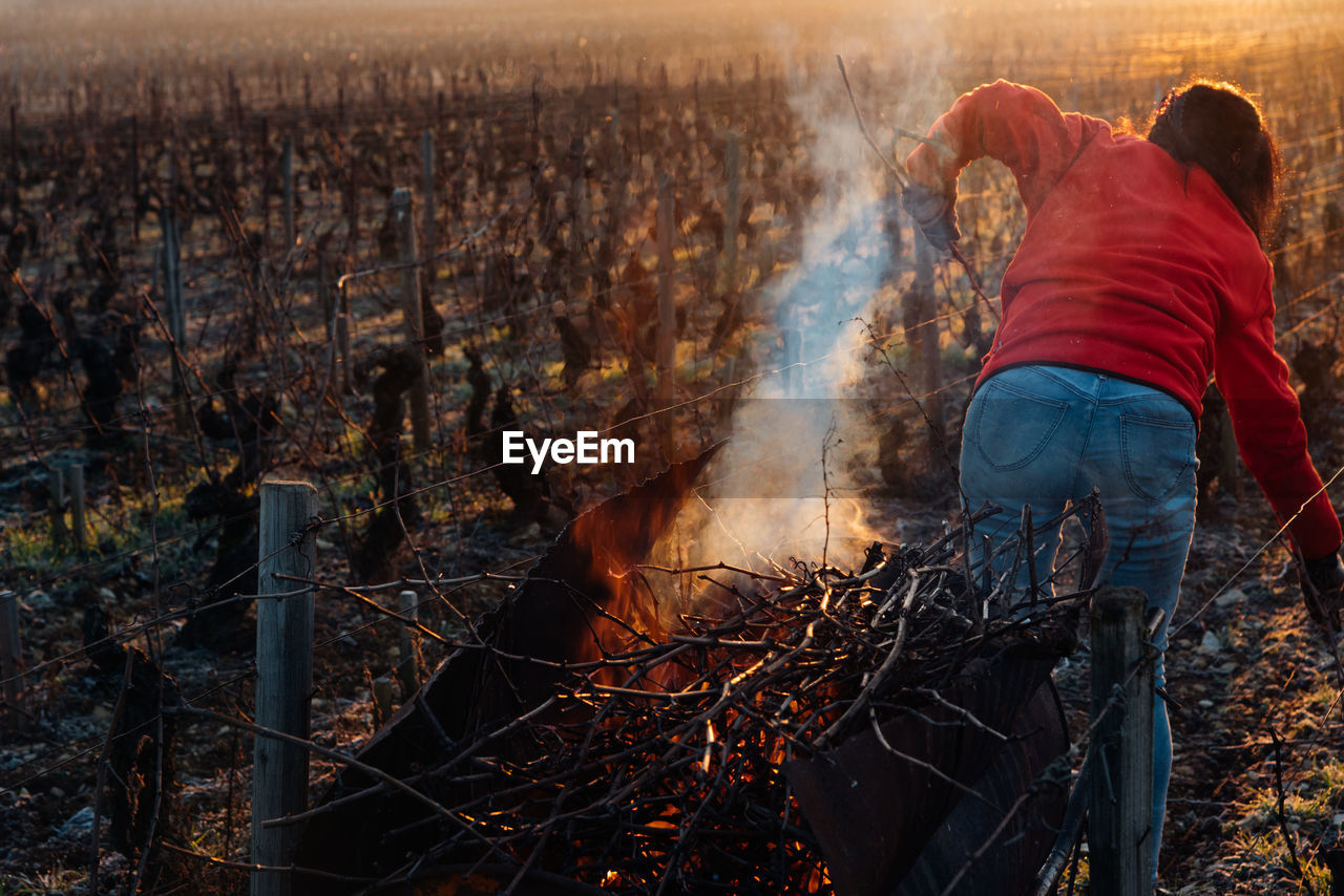 REAR VIEW OF PEOPLE STANDING BY BONFIRE ON LAND