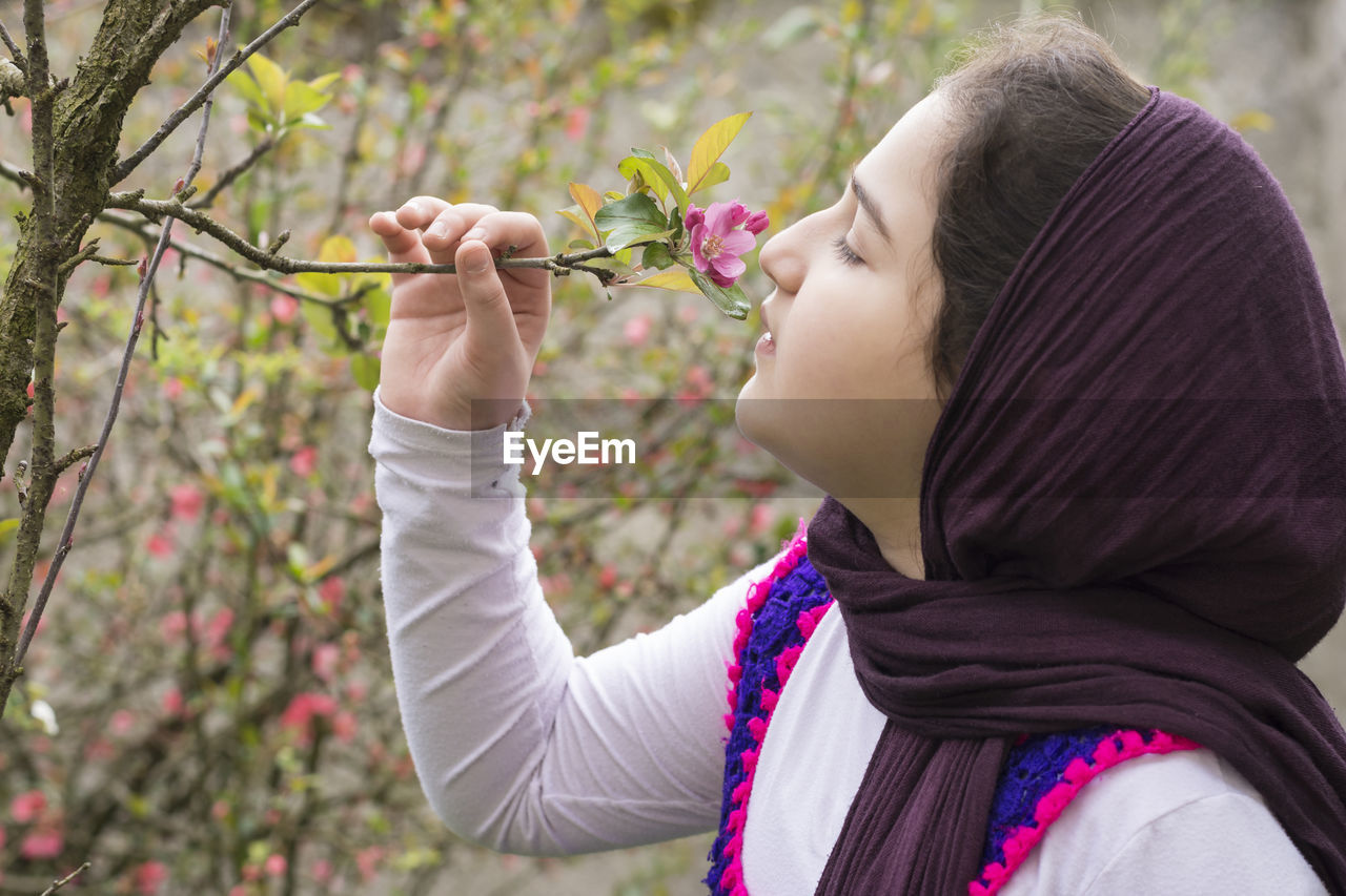 Side view of girl smelling flower on plant