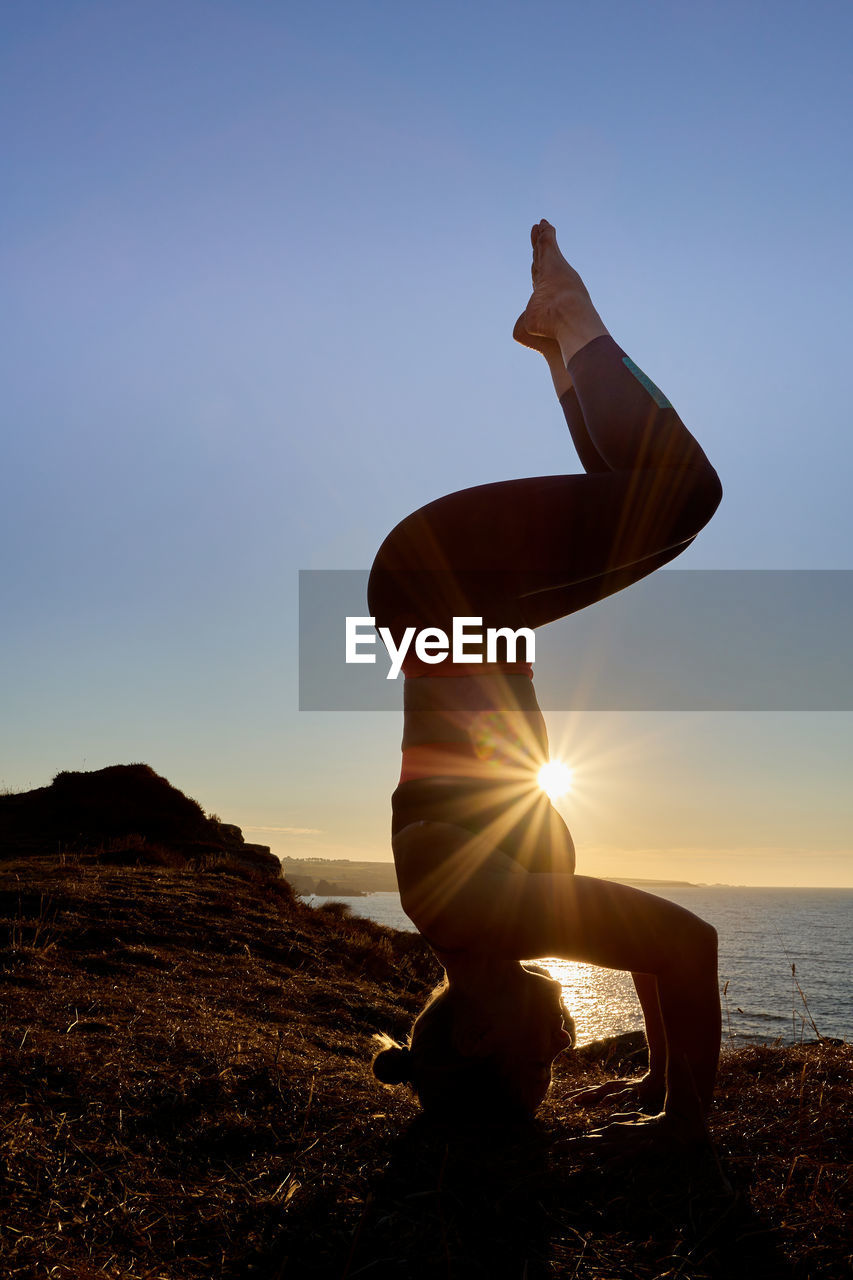 Inverted yoga pose of a woman at sunrise outside with a sun star.