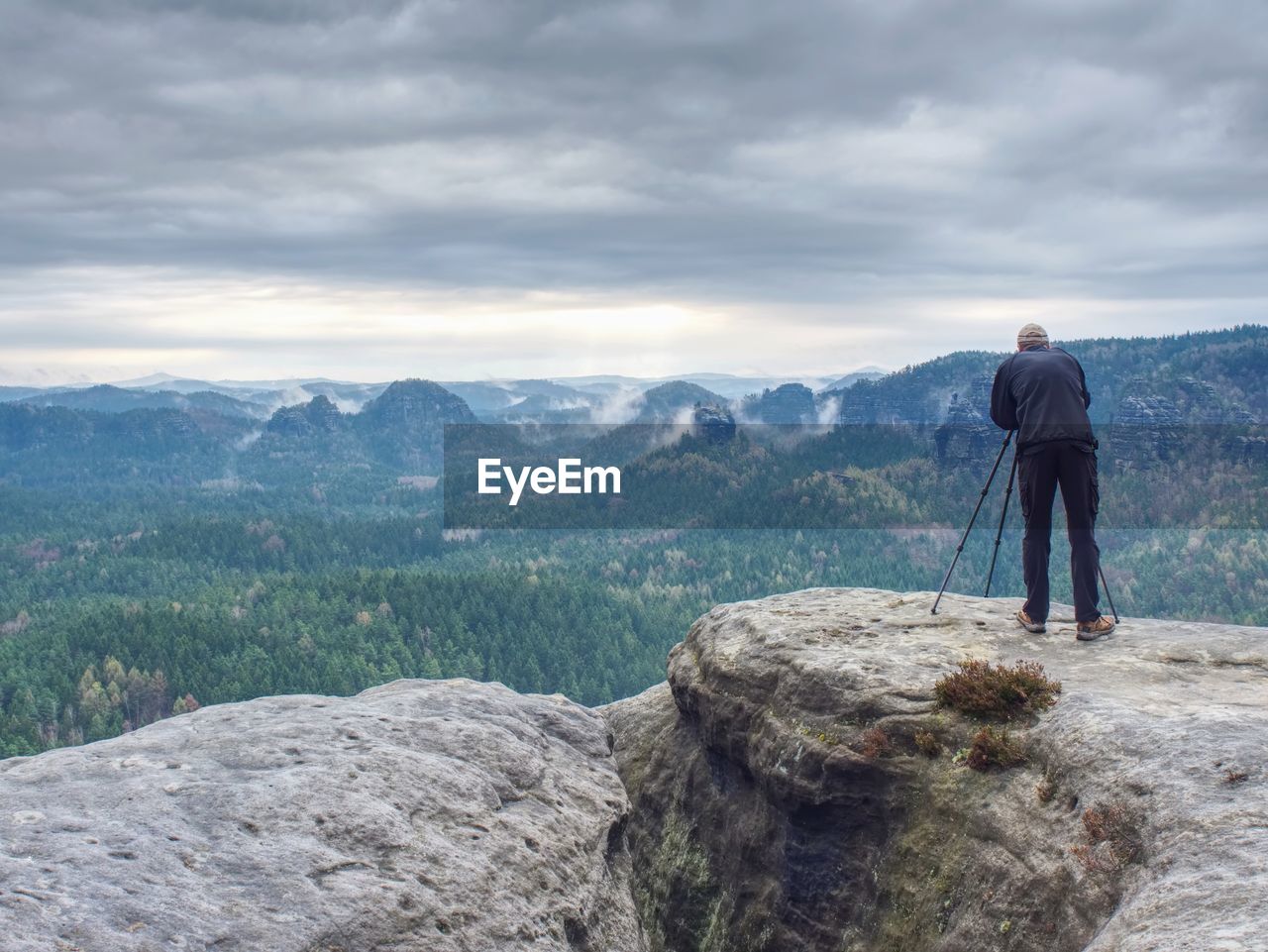 Photographer check display of camera on tripod. man stay on cliff and takes photos talk friends.