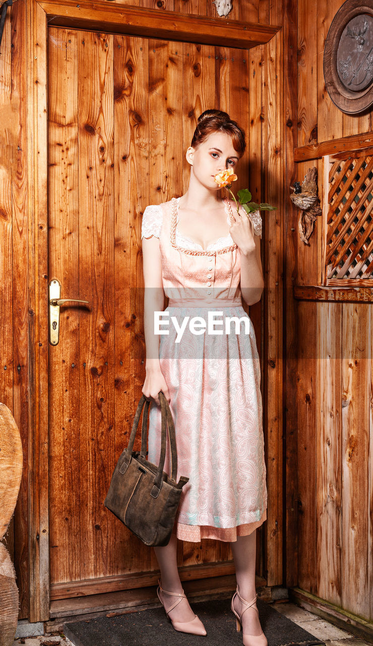 Portrait of young woman standing against wooden door