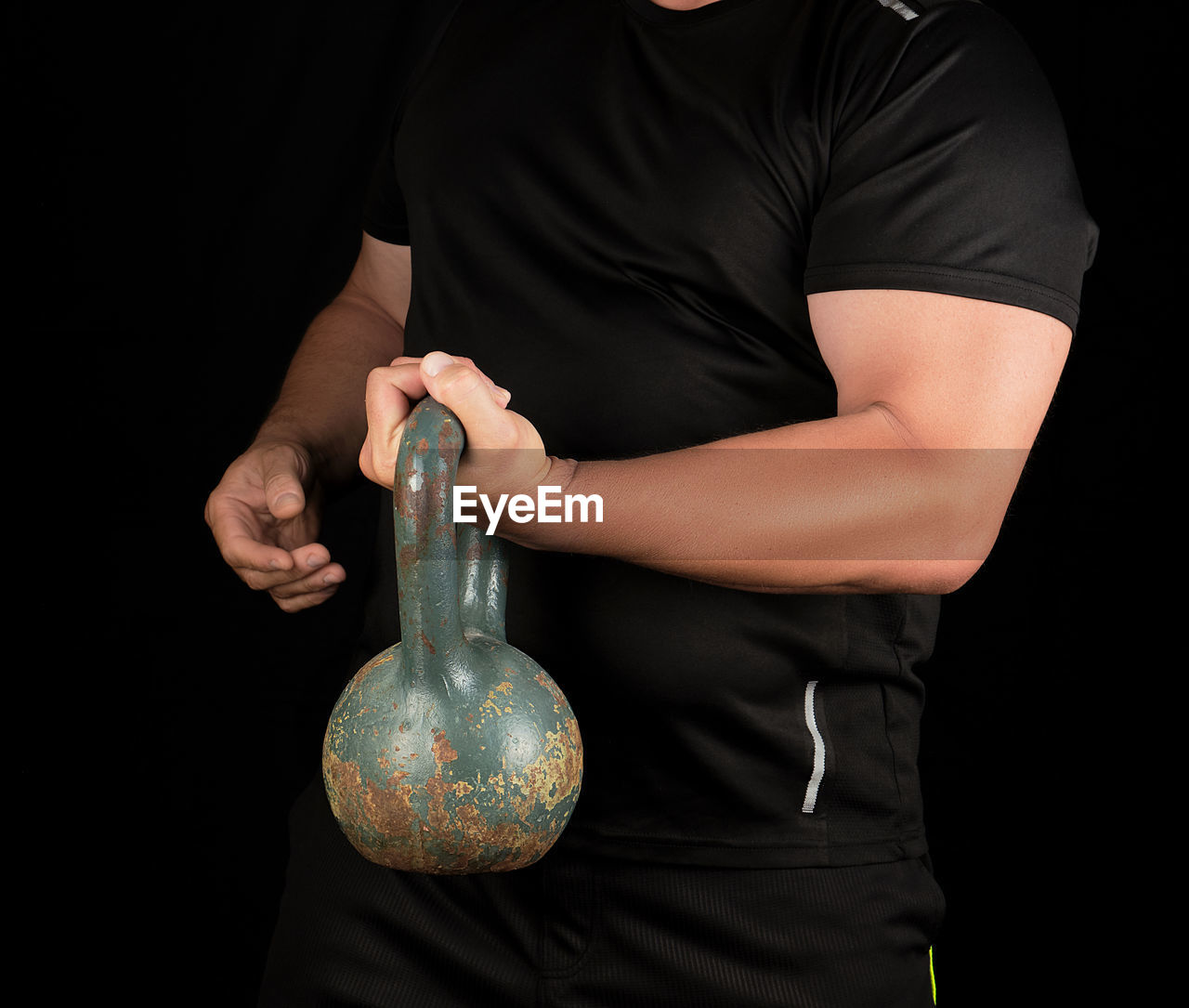 Midsection of man lifting kettlebell against black background