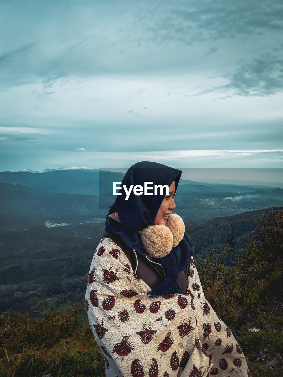 Woman wrapped in blanket looking away while standing against mountains