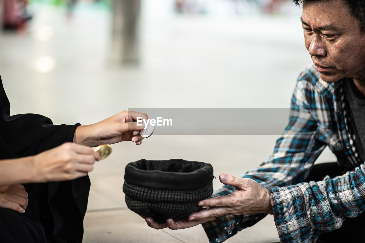 Cropped hands putting coins in hat held by beggar