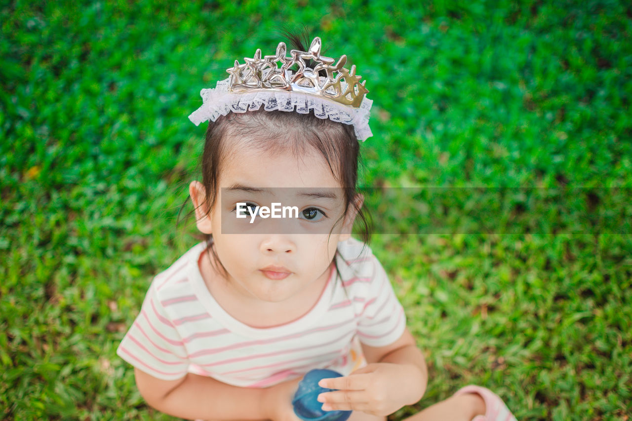 High angle portrait of cute girl wearing tiara while sitting on grassy field at park