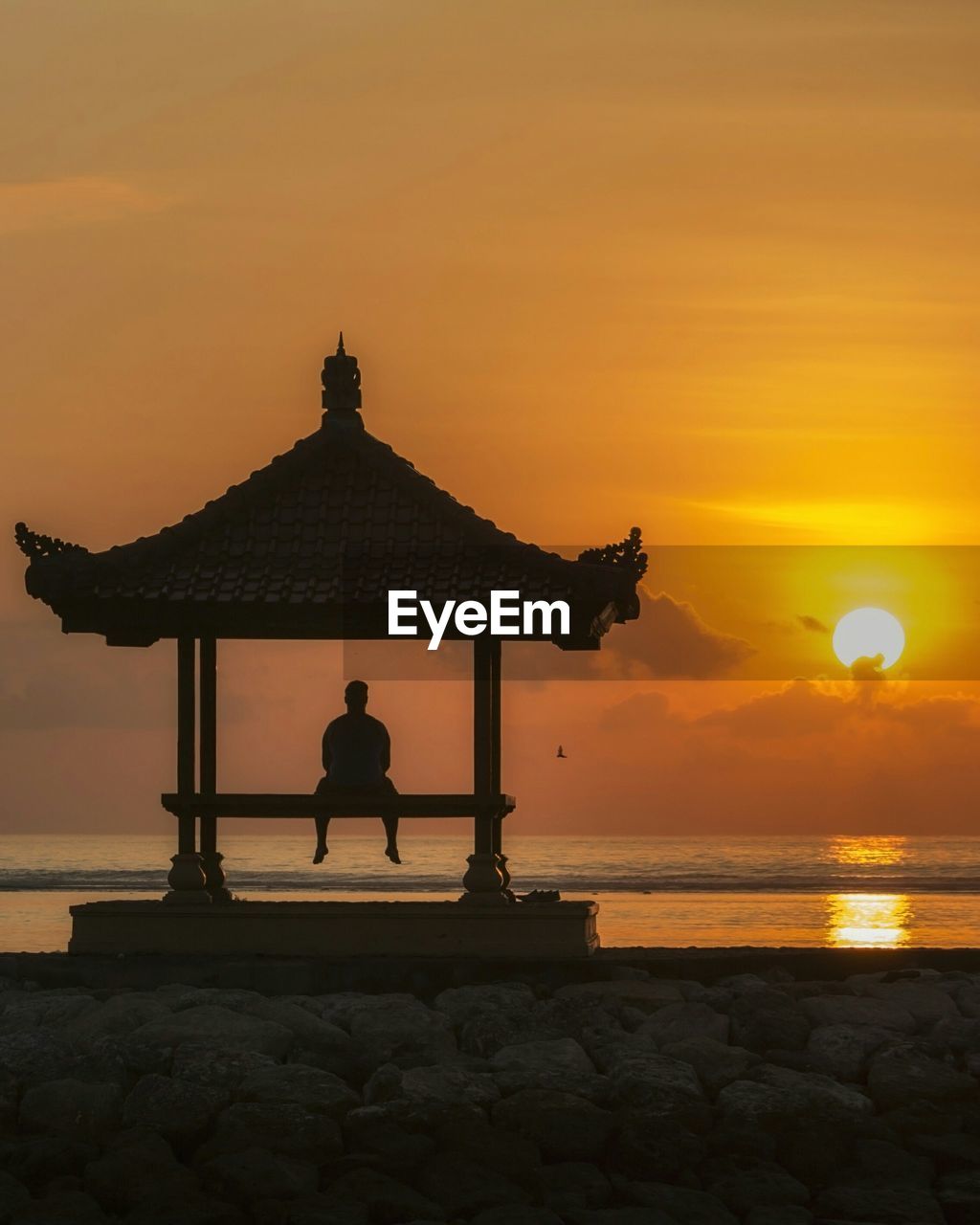 Silhouette man sitting in gazebo at beach during sunset
