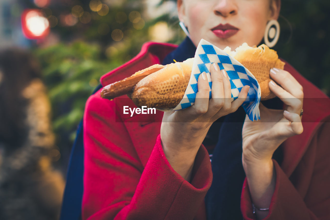 Close-up of a girl holding a long grilled bavarian sausage served in white bread.