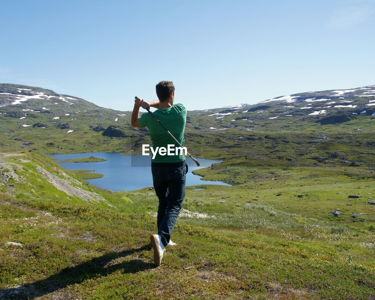 Rear view of man playing golf on hill against sky