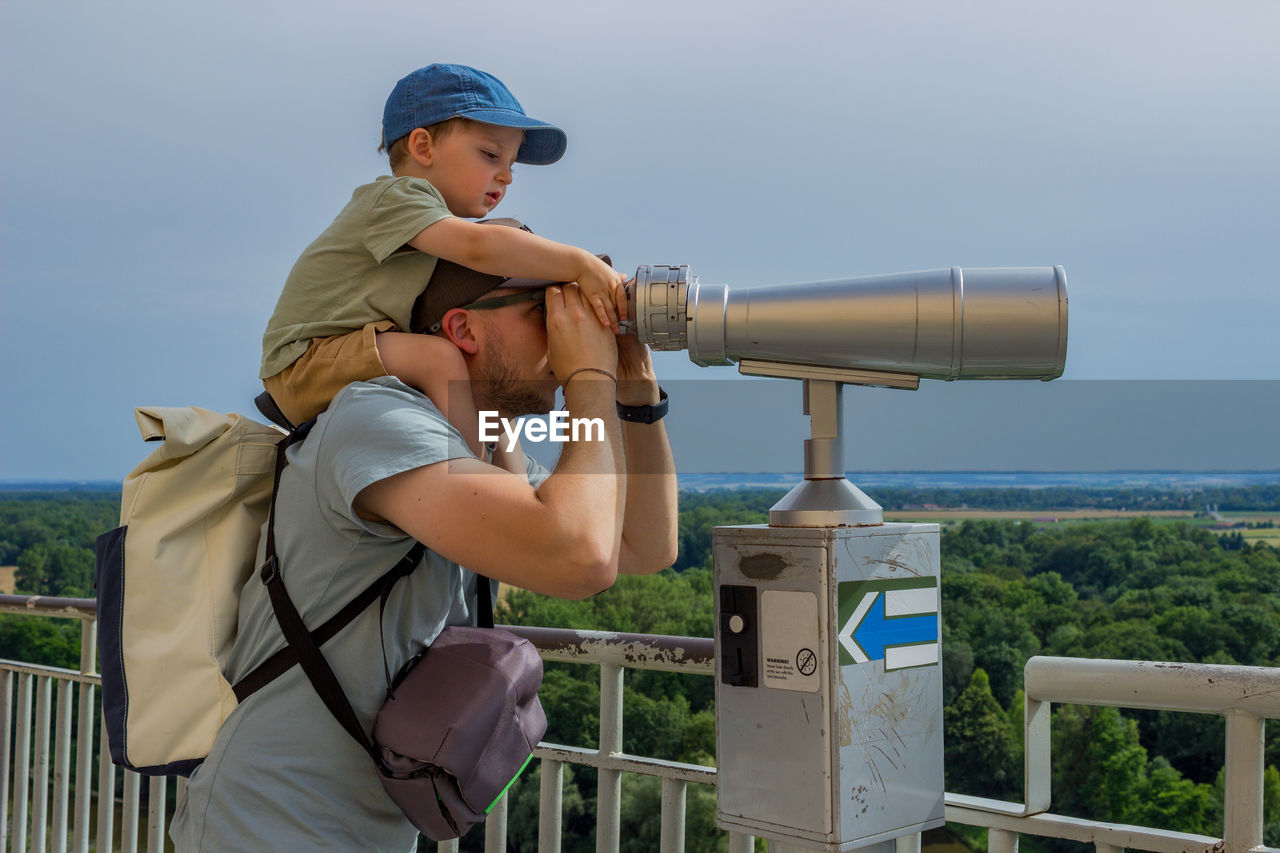 side view of man photographing through binoculars against clear sky