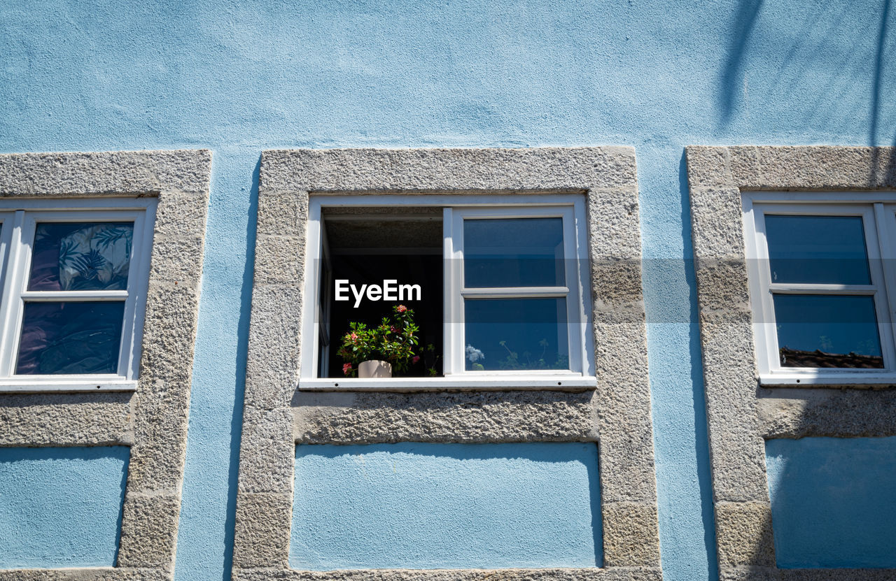 Blue house facade with an open window and flowers on the windowsill.