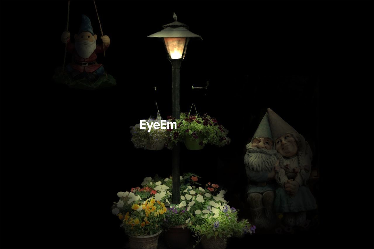 Illuminated lamp with flower baskets and statues against black background
