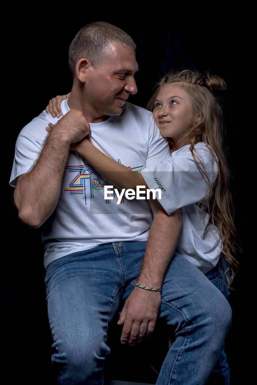 Full length of father and daughter against black background