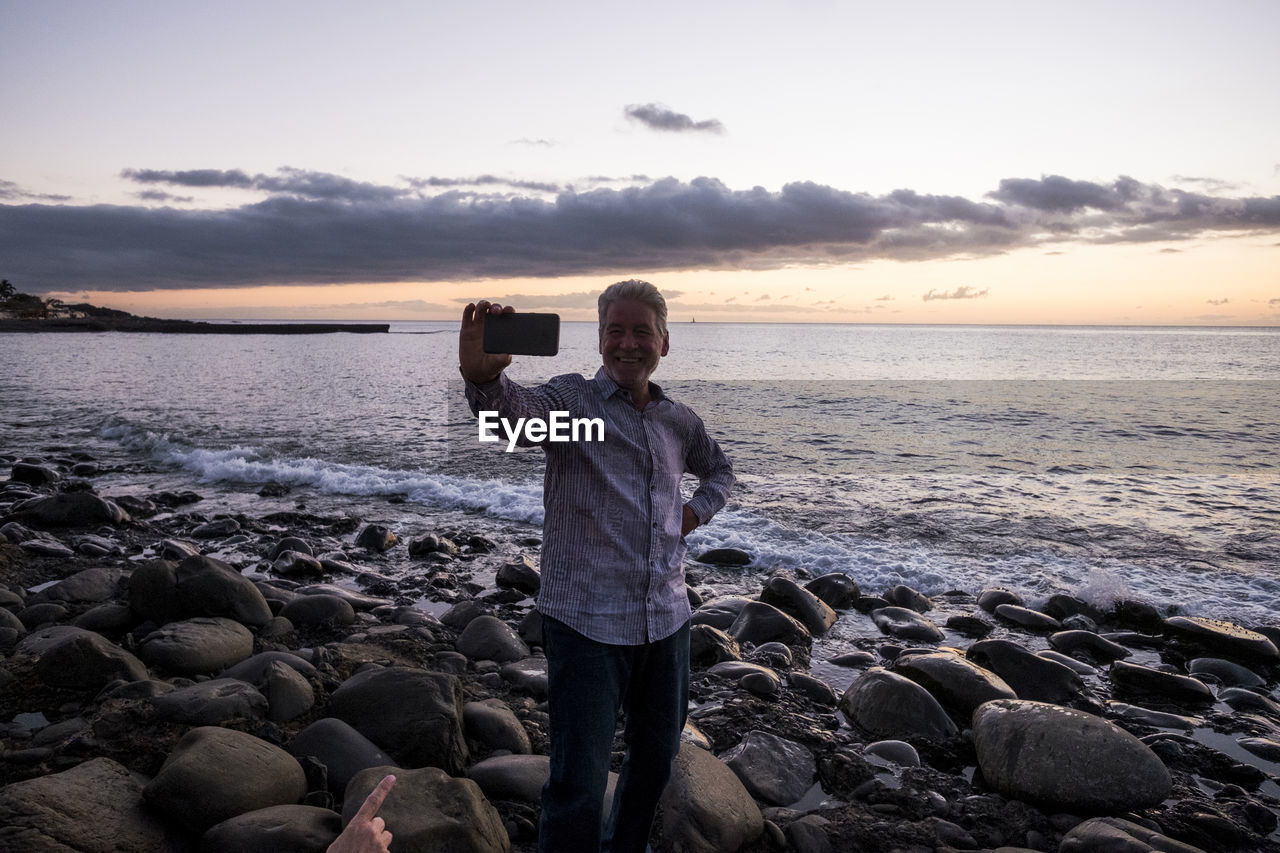 Man photographing from mobile phone at beach during sunset