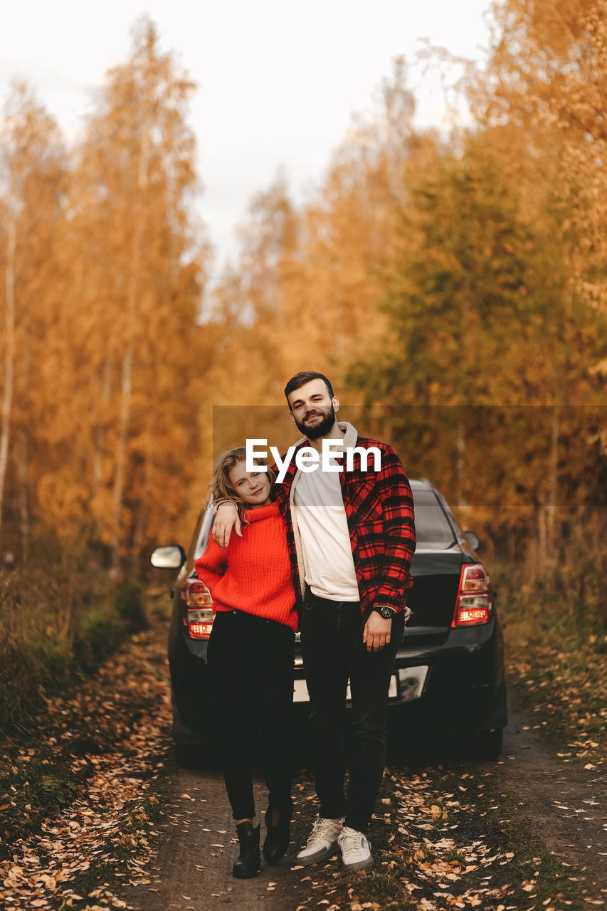 PORTRAIT OF YOUNG COUPLE STANDING ON AUTUMN TREES