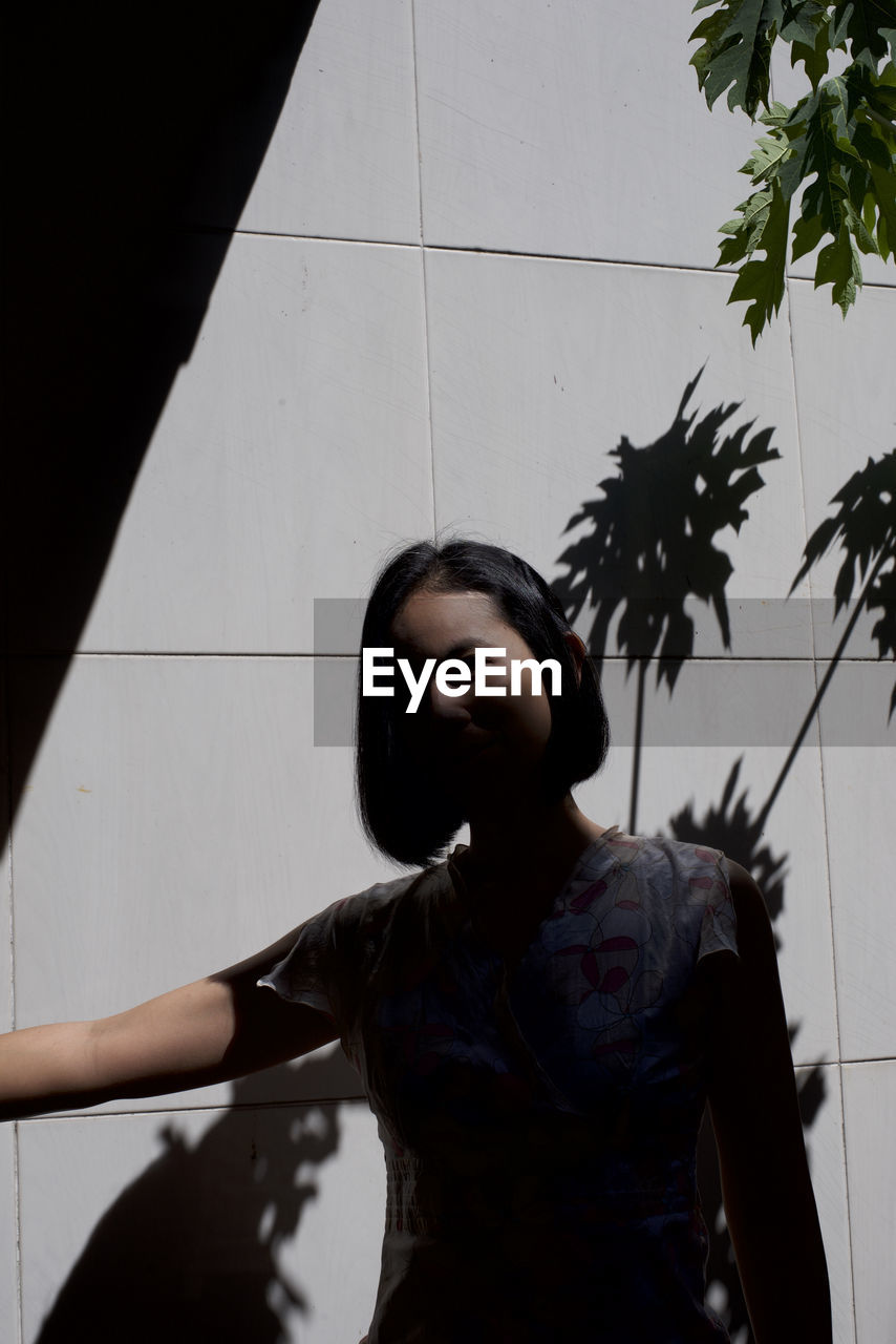 Woman standing in tree shadow against wall