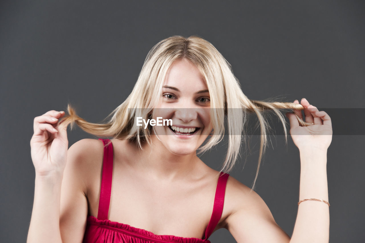 Portrait of happy woman holding hair against black background