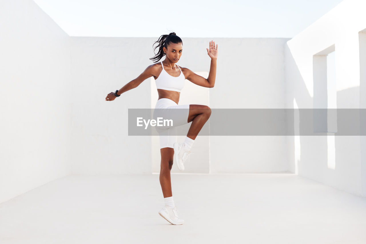 full length of young woman standing against white wall