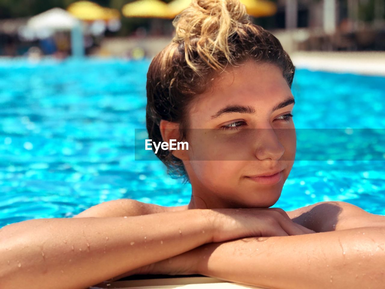 Wet thoughtful teenage girl looking away while swimming in pool