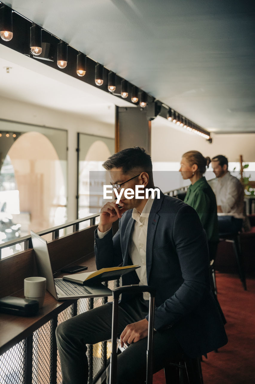 Businessman with hand on chin looking at laptop in hotel