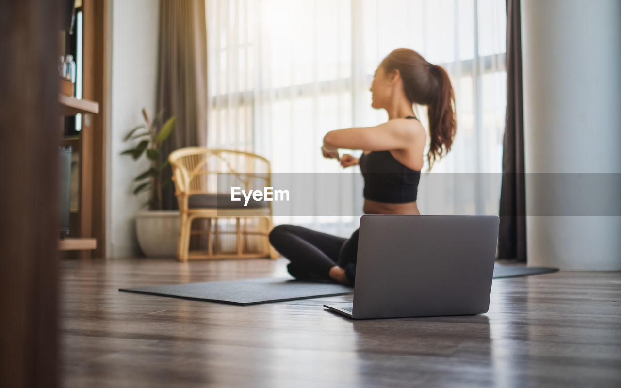 Young woman using laptop while sitting on hardwood floor at home