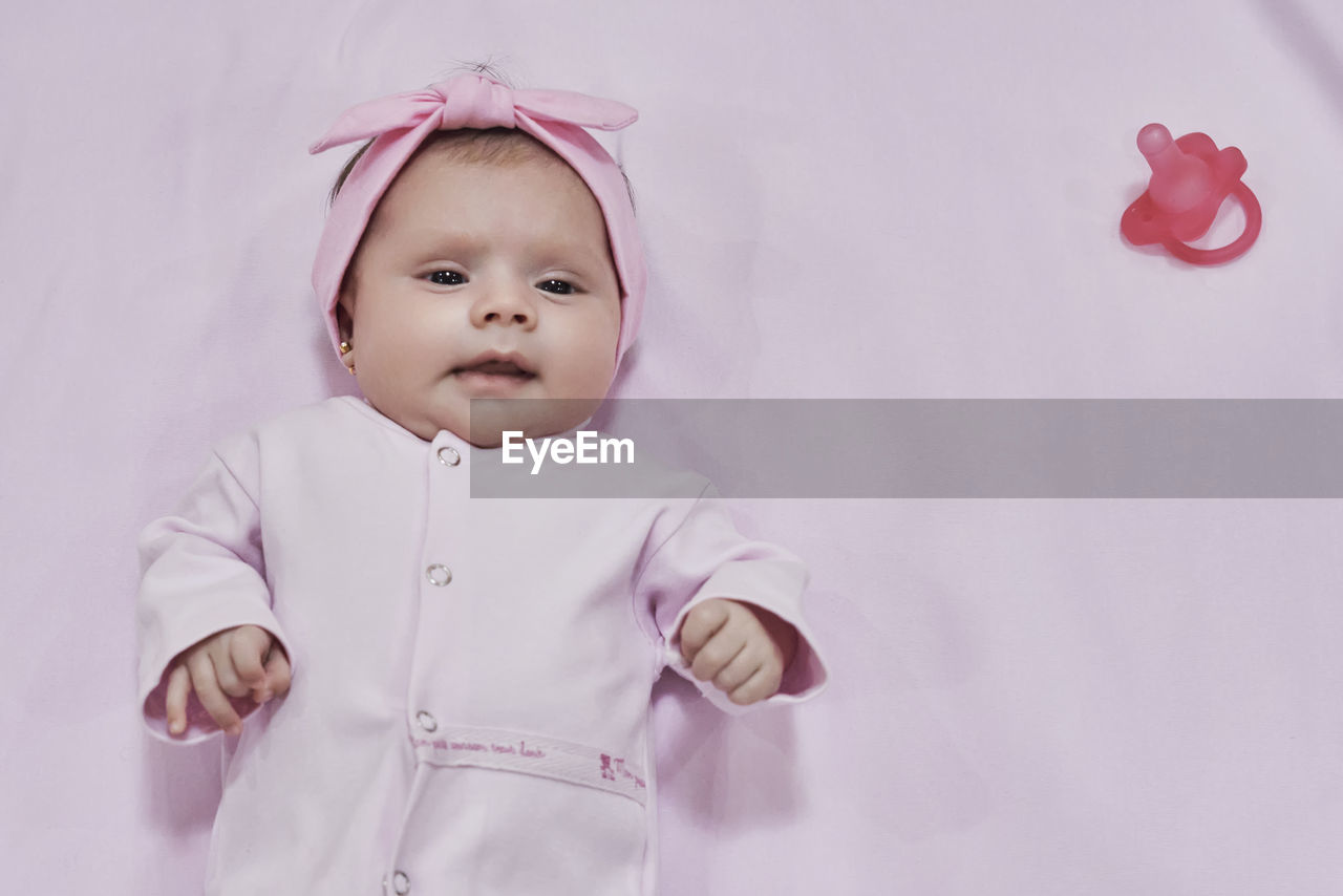 Portrait of cute baby girl with arms crossed standing against wall