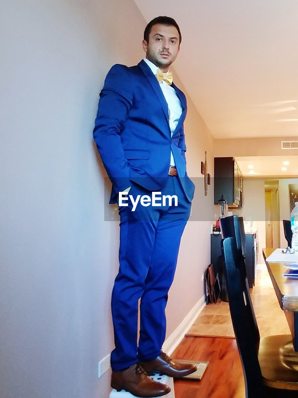 Portrait of young man wearing suit standing on stool in room