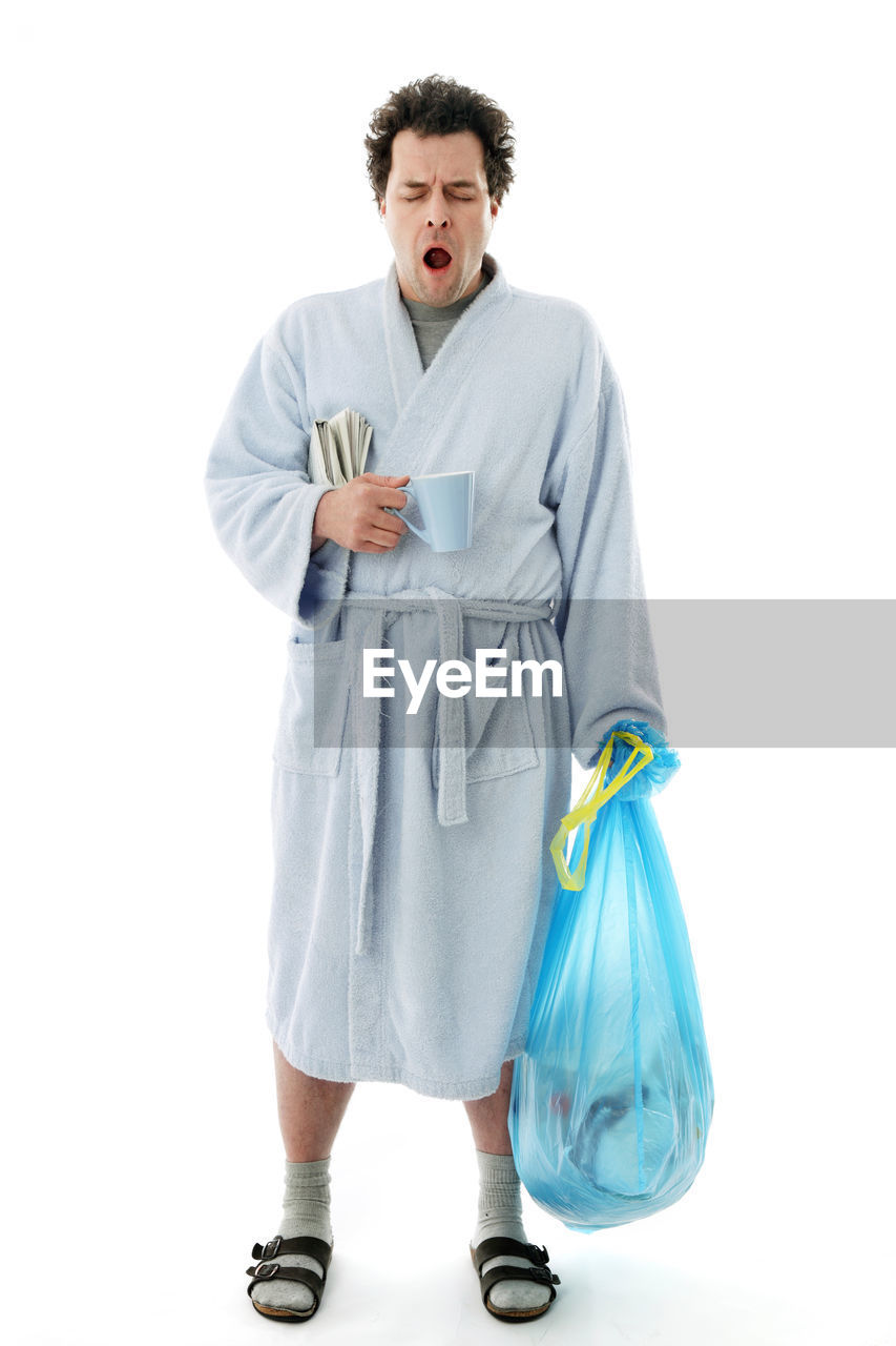 Man in bathrobe yawning while standing against white background