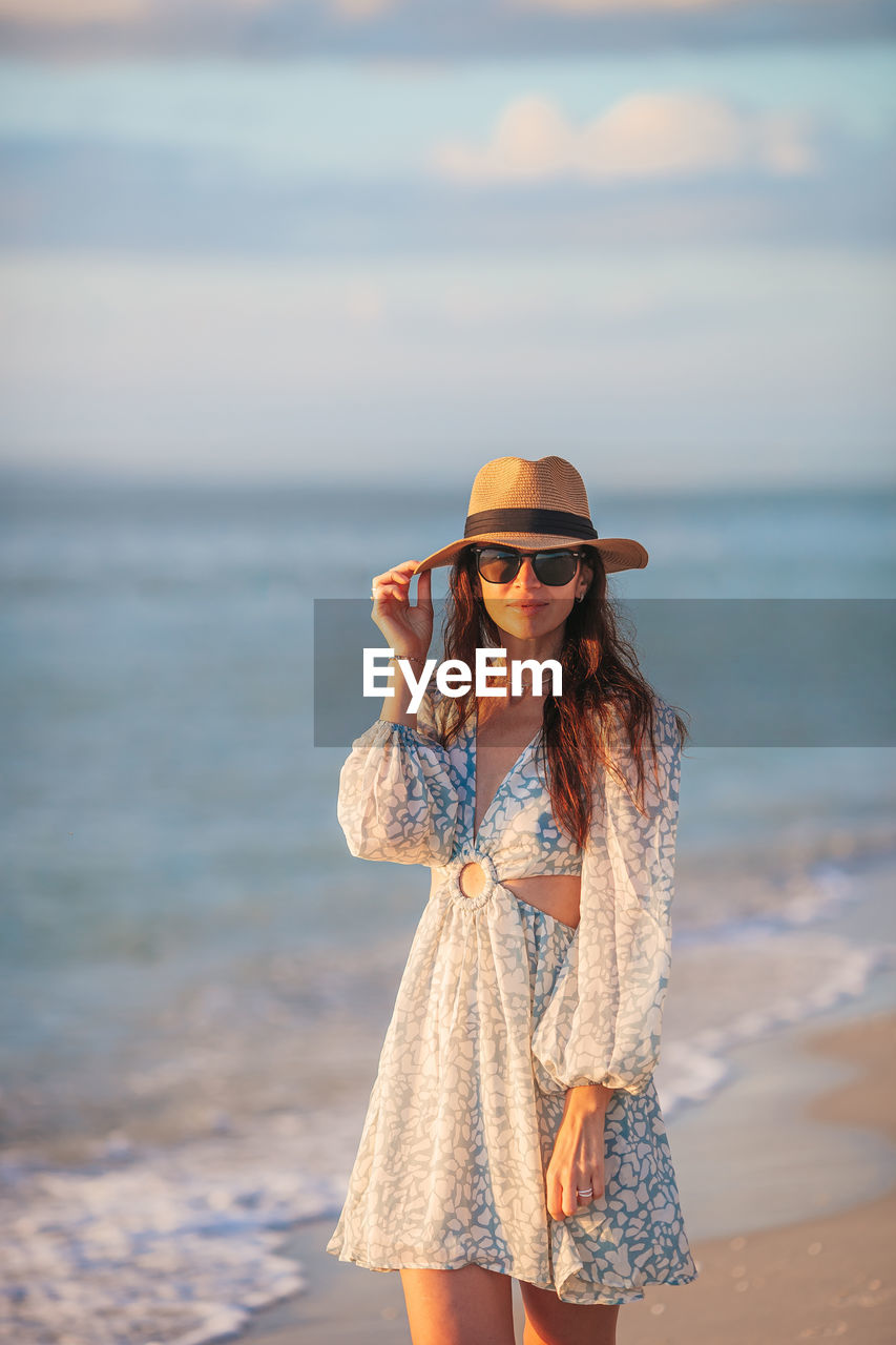 portrait of young woman wearing hat standing at beach